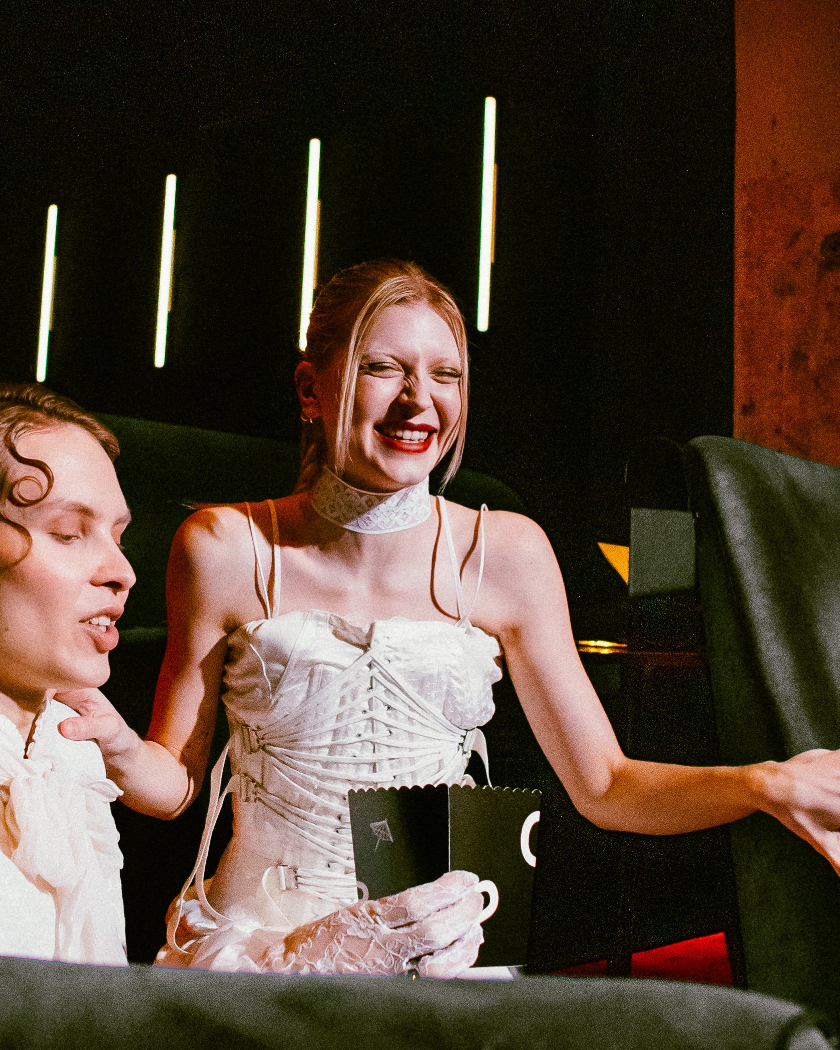 Kaksi nuorta aikuista juhlatunnelmassa, toinen pitelee lahjakorttia – lämmin ja iloinen hetki, joka esittelee verkkokaupan lahjakortin lahjaideana.